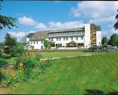 A modern hotel building surrounded by a well-maintained lawn and green plants. The sky is blue with some clouds.