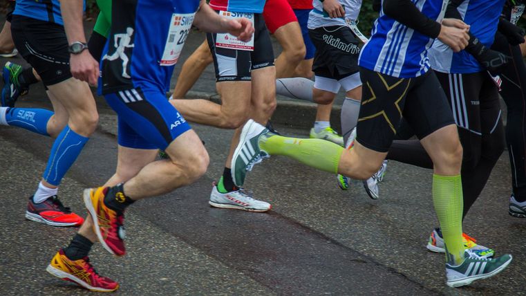 Un groupe de coureurs en tenue de sport se déplace rapidement sur la route. Les pieds et les jambes des participants sont clairement visibles alors qu'ils prennent part à une course.