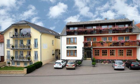 A small hotel with two buildings and balconies. In front of the hotel, there are some cars and the sky is partly cloudy.