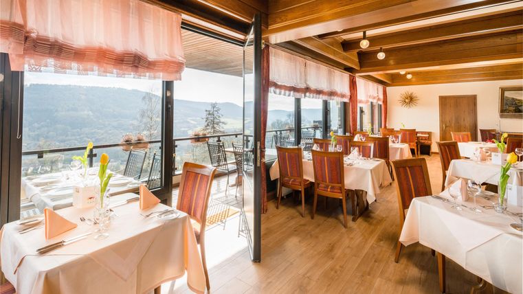 Ein elegantes Restaurant mit hellen Tischen und komfortablen Stühlen. Große Fenster bieten einen schönen Ausblick auf die Landschaft.