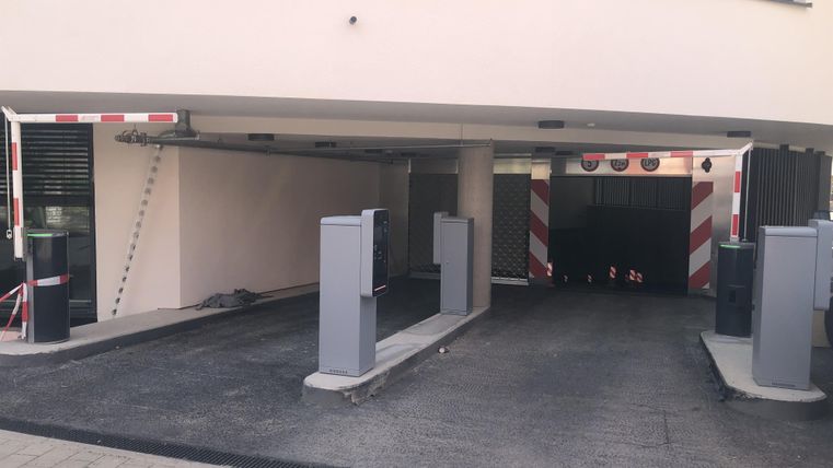 Eine Garageneinfahrt mit Schranken und Pollern. Der Boden ist befestigt und sichtbar ist ein geschlossener Bereich dahinter.