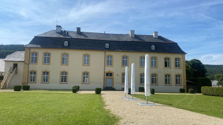 A beautiful yellow building with several windows and a well-maintained garden. In the foreground, there are some modern sculptures.