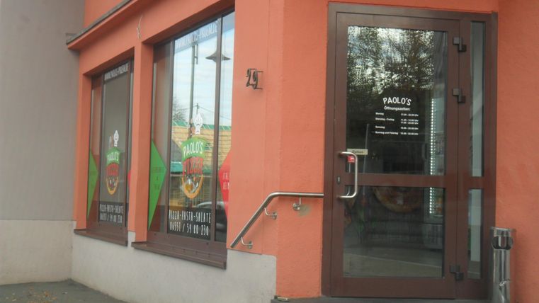 Ein Restaurant namens "Pablo's" mit großen Fenstern und einer einladenden Eingangstür. Die Wände sind orange gestrichen und es gibt Informationen über die Öffnungszeiten an der Tür.