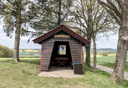 Une petite cabane en bois avec un panneau 'Knutschheisjen' se trouve entre les arbres dans un paysage verdoyant de champs et de collines., &copy; A. Girards
