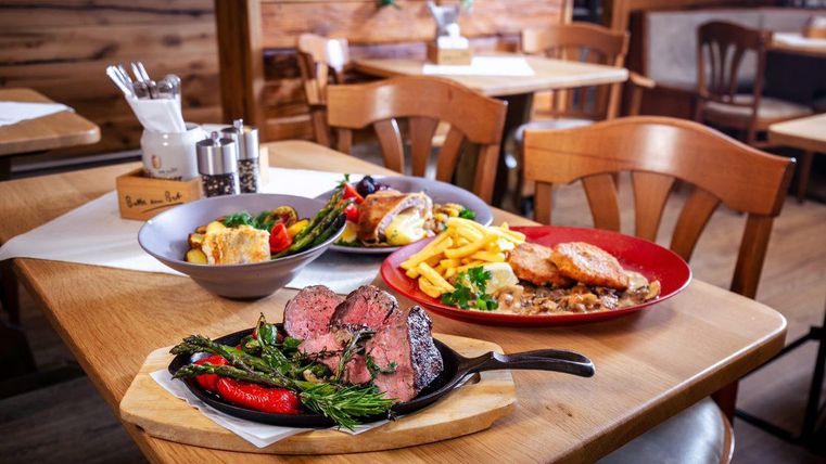 A rustic table with delicious dishes. In the foreground, a juicy steak with vegetables, next to fries and other sides.