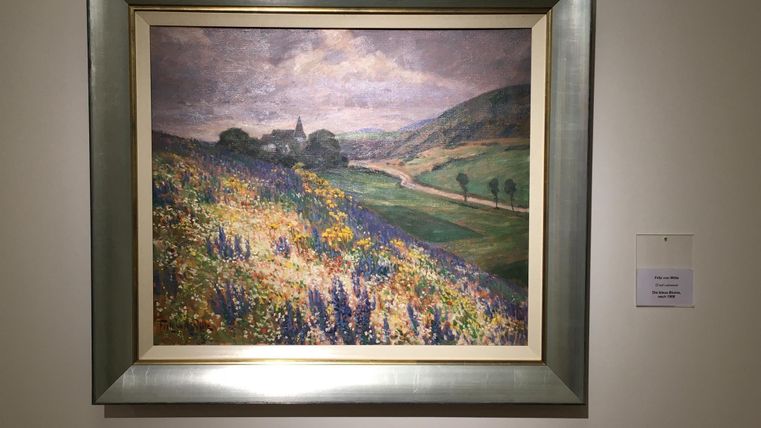 An Impressionist painting of a landscape with gentle hills and blooming meadows. In the background, trees and a narrow path are visible.