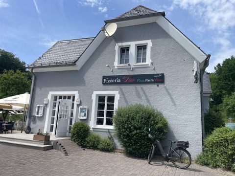 Un restaurant de pizza confortable avec une façade grise et une entrée accueillante. Devant le bâtiment se trouvent un vélo et quelques plantes.