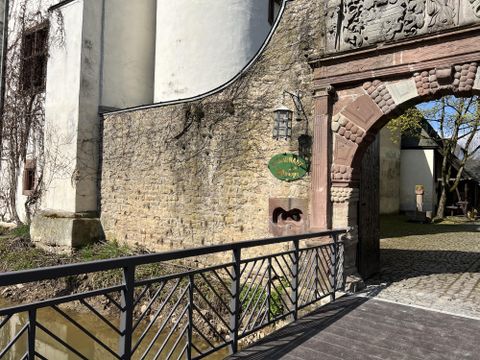 Een historisch gebouw met een mooie stenen façade en een romantische poort. Een brug leidt over een klein stroompje naar de ingang.