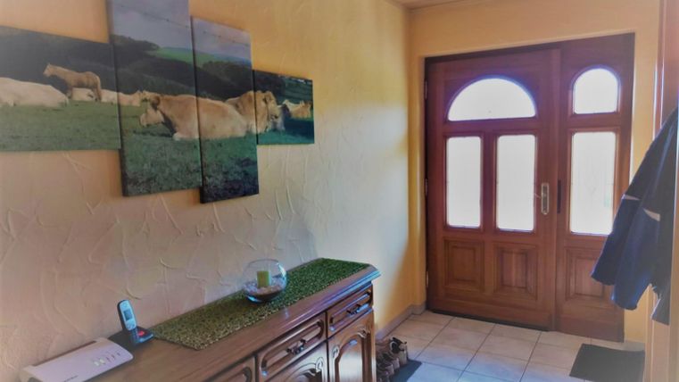 An inviting hallway with wood decor and a large front door. On the wall, there are pictures of cows in a rural landscape.