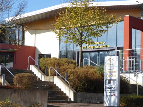 Een modern evenementen- en congrescentrum met een grote glazen pui. Voor het gebouw bevinden zich trappen en een verzorgd groenvoorziening.