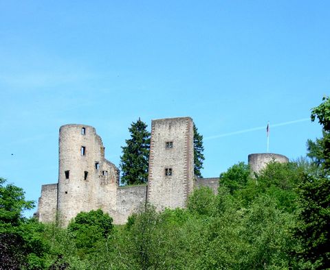 An old castle sits on a hill, surrounded by lush greenery. The sky is blue and clear.