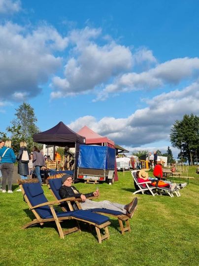 A cozy green space with loungers under a blue sky. In the background, people and tents can be seen.