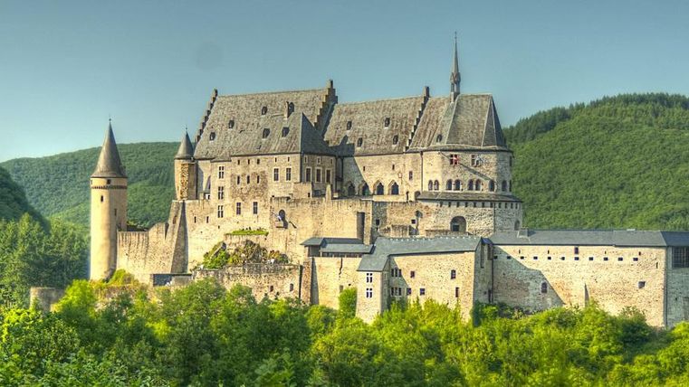 An impressive castle surrounded by green hills. The clear sky and picturesque landscape give the place a fairytale atmosphere.