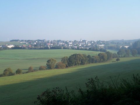 Een schilderachtig landschap met glooiende heuvels en een klein dorp op de achtergrond. De lucht is helder en zonnig.