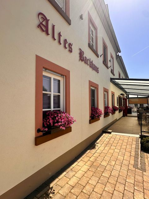 Ein charmantes Gebäude mit der Aufschrift "Altes Bachhaus". Blumenkästen mit bunten Blumen schmücken die Fenster.