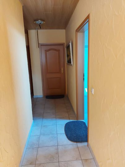 A bright hallway with yellow walls and tiled floor. At the end of the hallway, there are two doors and a carpet in front of one door.