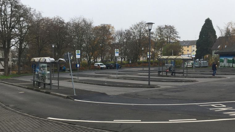 Ein leerer Parkplatz mit mehreren Bushaltestellen. Die Umgebung ist bewaldet und die Sicht ist durch Nebel eingeschränkt.
