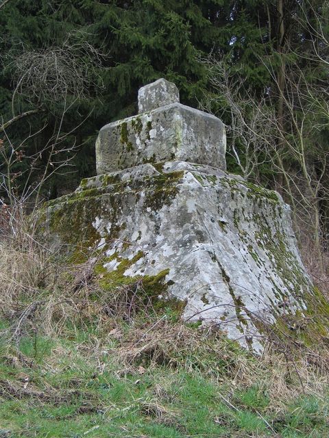 A large, moss-covered rock with a square structure on top. Surrounded by greenery and trees in a tranquil setting.