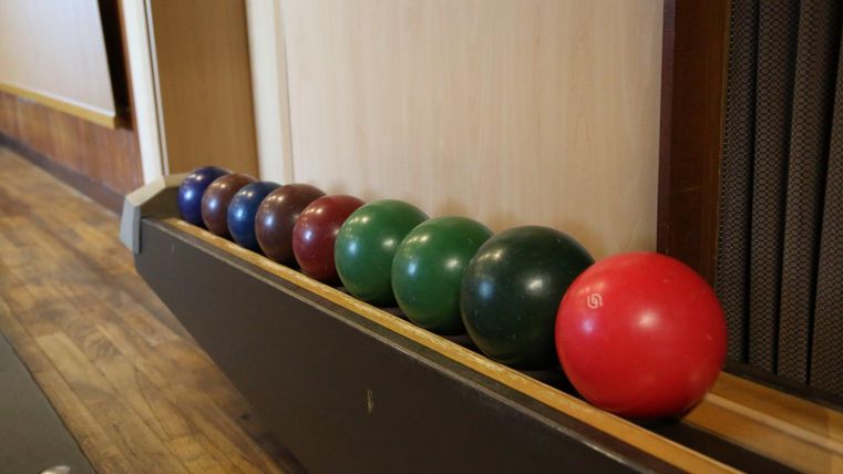 Eine Reihe bunter Bowlingkugeln steht auf einer Holzoberfläche. Die Kugeln sind in verschiedenen Farben angeordnet, darunter Blau, Grün, Rot und Braun.