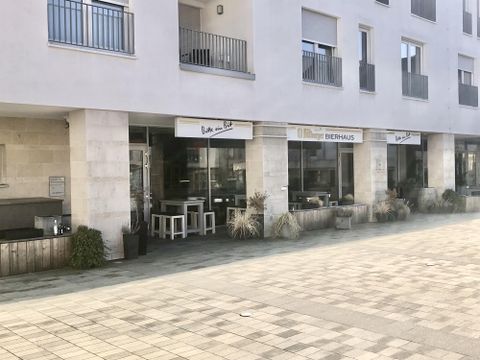 Ein modernes Gebäude mit Glasfronten und mehreren Geschäftseinheiten. Draußen stehen Tische und Pflanzen, die eine einladende Atmosphäre schaffen.