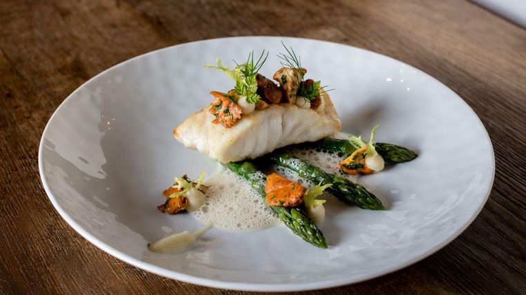 A beautifully arranged plate with fried fish, garnished with mushrooms and herbs. Served with fresh green asparagus.