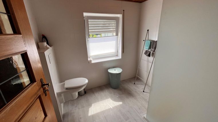 Een moderne badkamer met een wit toilet en een groene wc. De kamer heeft lichte tegels en een houten plafond.