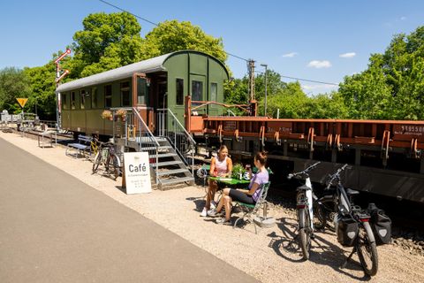 Een gezellige caféscene naast een voormalige treinwagon. Twee personen zitten buiten en genieten van hun verblijf, terwijl fietsen in de buurt geparkeerd staan.