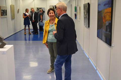 An art exhibition with several visitors. Two people are standing in the foreground and talking.