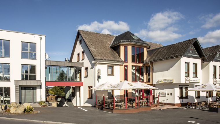 Ein modernes Gebäude kombiniert mit traditioneller Architektur. Vor dem Haus befinden sich Terrassen mit Sonnenschirmen.