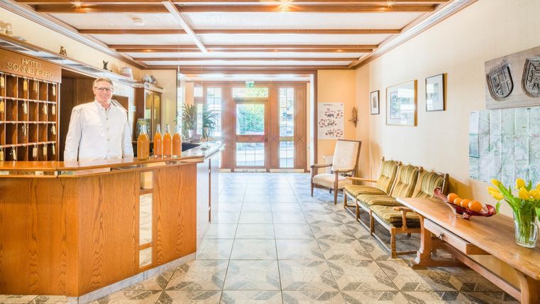 Eine einladende Lobby mit einem Empfangstresen aus Holz. Im Hintergrund sind bequeme Sitzgelegenheiten und Dekorationen zu sehen.