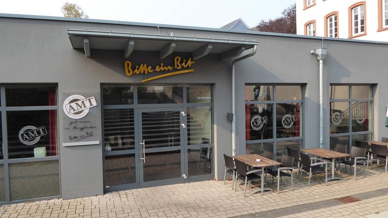 Een modern restaurant met grote ramen en een uitnodigende buitenruimte. Tafels staan op de stoep, klaar voor gasten.