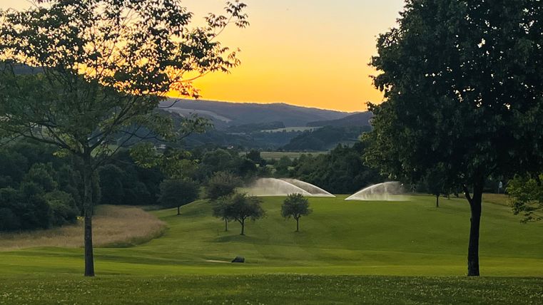 Eine malerische Golfanlage im Sonnenuntergang. Sprinkler bewässern das grüne Gras und die Umgebung ist friedlich und schön.