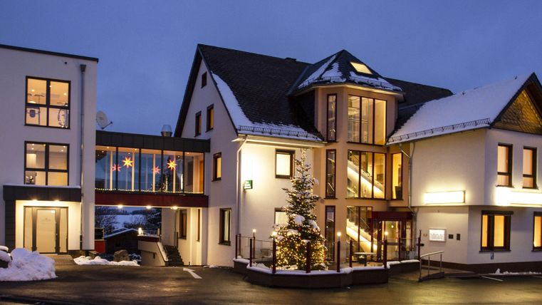 A modern building at dusk, surrounded by snow. The warm lights of the windows radiate an inviting atmosphere.