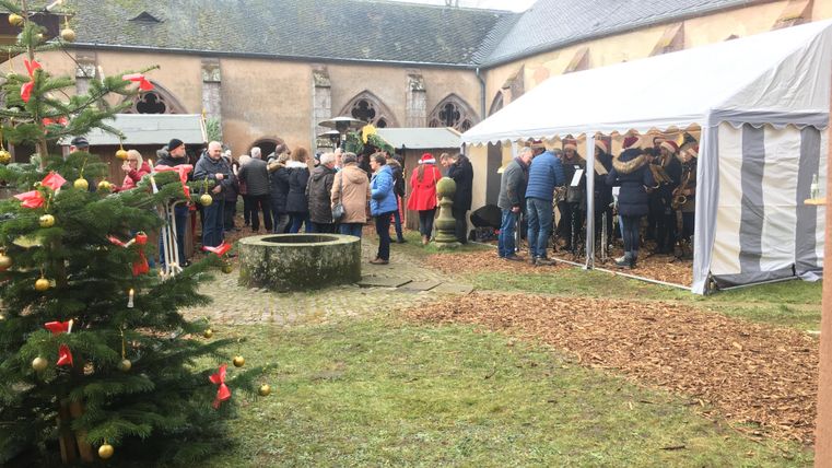 Un événement festif en plein air avec une grande foule sous un chapiteau. Au premier plan, il y a un sapin de Noël avec des décorations rouges.