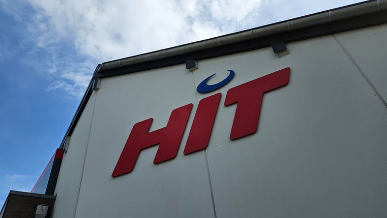A part of a building with the red logo "HIT". The sky in the background is partly cloudy.