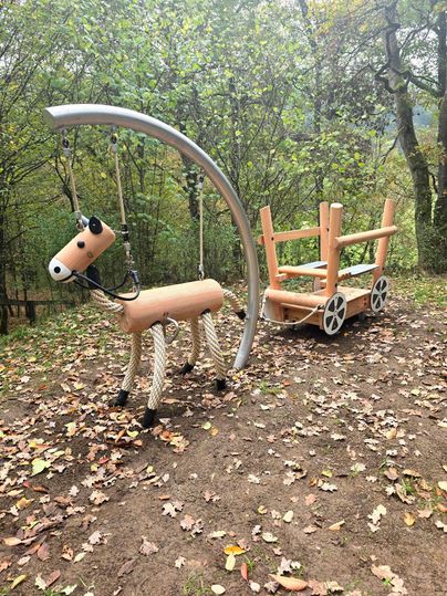 Un terrain de jeu avec un cheval en bois et une charrette. L'environnement est marqué par des arbres et des feuillages d'automne.