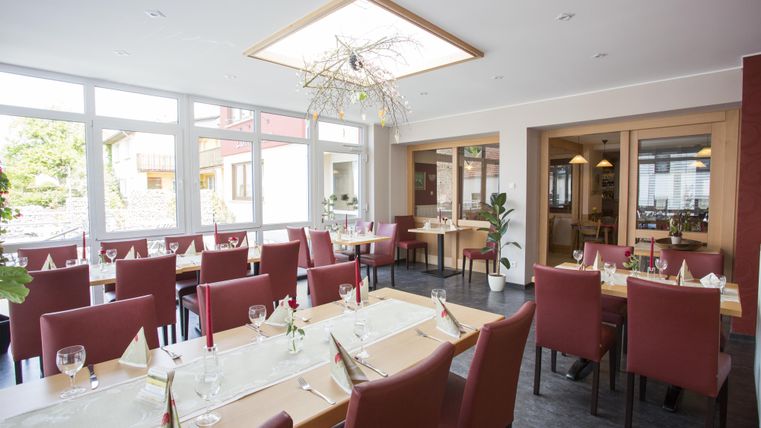 An elegant restaurant with red chairs and large windows. The table is beautifully set, and there is modern lighting.