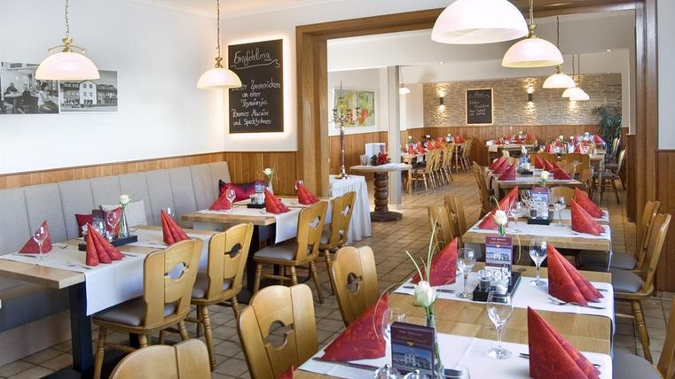 A cozy restaurant with wooden furniture and beautifully set tables. Red cloth napkins and an inviting atmosphere create a pleasant ambiance.