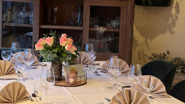 An elegantly set table with cloth napkins and glass dishes. In the center stands a floral arrangement with pink roses.