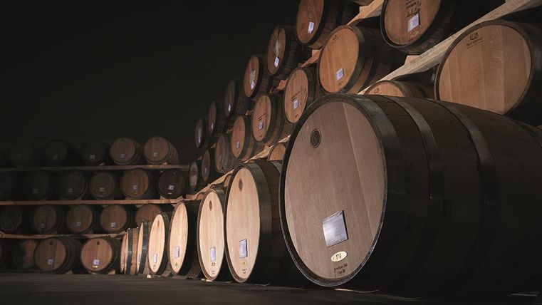 Een opslagruimte met meerdere houten vaten die bovenop elkaar zijn gestapeld. De vaten zijn goed verlicht en staan op een wandloze oppervlakte.