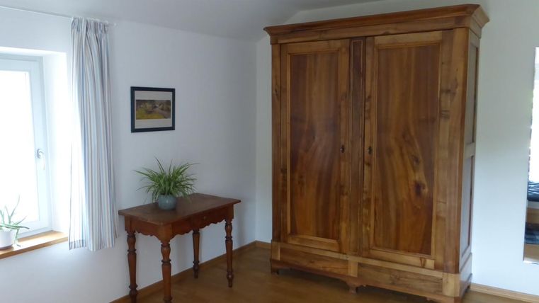A cozy room with a large wooden cabinet and a small table. The windows let in a lot of natural light.