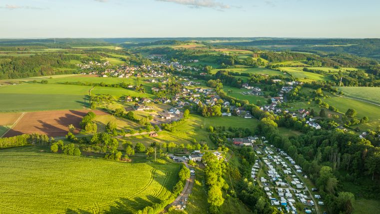 Luftaufnahme einer grünen Landschaft mit Feldern, einem Dorf und einem Campingplatz.