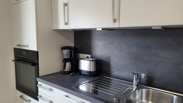 A modern kitchen with white cabinets and a dark countertop. There is a sink, a kettle, and a coffee maker.