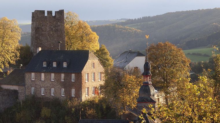 A historical building view with an old tower and colorful autumn trees. In the background, a gentle hilly landscape stretches out.