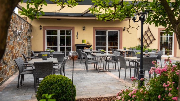 Een gezellige patio met zitplaatsen en tafels. Omringd door groene planten en kleurrijke bloemen.