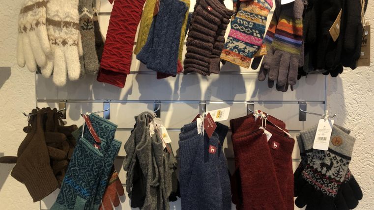 Une sélection de différents gants dans des couleurs et motifs variés est accrochée à un mur. Les gants sont bien visibles et triés.