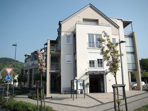 A modern building with clean lines and large windows. Planted areas and a small street are visible in front of the building.