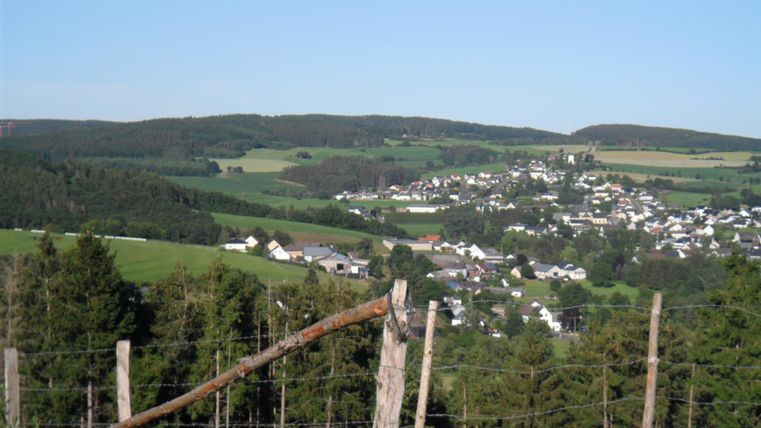 Un paysage pittoresque avec des collines et un petit village dans la vallée. Au premier plan, on voit des prairies et des piquets de clôture.