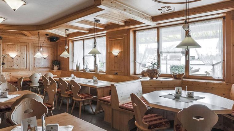 Une salle à manger confortable avec des meubles en bois et de grandes fenêtres. Les tables sont dressées avec des nappes blanches et des éléments décoratifs.
