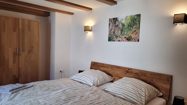 A cozy bedroom with a double bed and striped bed sheets. A picture of a natural landscape hangs on the wall, and there are wooden cabinets.